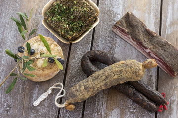 several variety of traditional Corsican charcuterie with an olive branch and black olives on wooden background