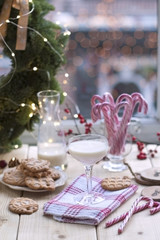 girl milk in a glass at the table by the window, cookies on a plate, and a wreath of Christmas tree