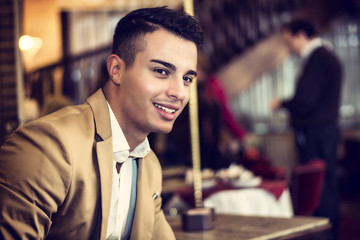 Portrait of smiling handsome man in jacket sitting at table with cup of drink looking at camera