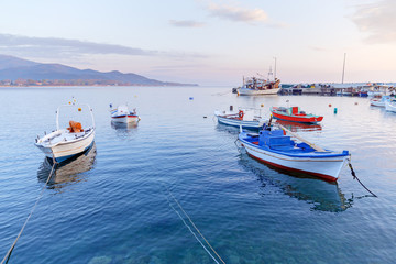 Naklejka na ściany i meble Greece, small port in coastal town Olimpiada (near Kavala) on Aegean sea. Dawn scenery of seafront. Fishing boats anchored to quay, beautiful morning landscape.