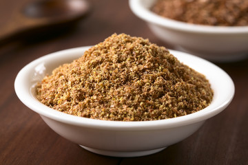 Ground or crushed brown flax seed or linseed in small bowl, photographed on dark wood with natural light (Selective Focus, Focus one third into the ground linseed) - obrazy, fototapety, plakaty