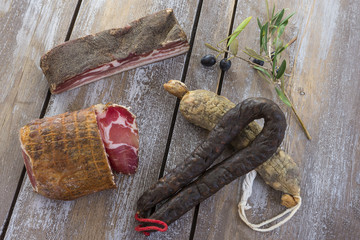 several variety of traditional Corsican charcuterie with an olive branch and black olives on wooden...
