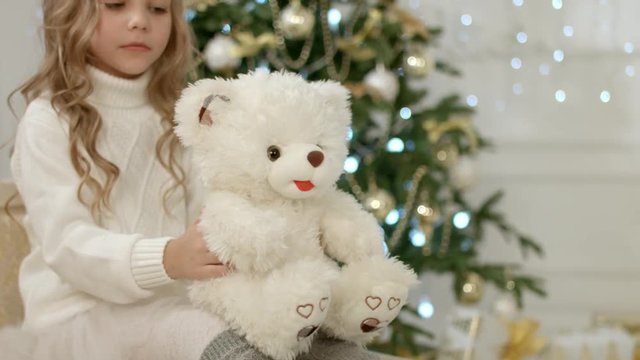 Portrait of the cute little girl playing with her soft toy near the Christmas tree