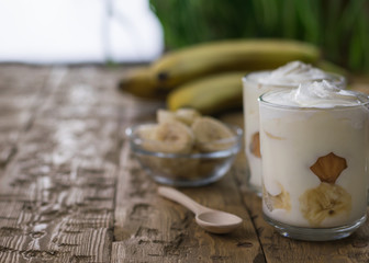 Banana dessert with whipped cream and biscuit on a dark wooden rustic table.