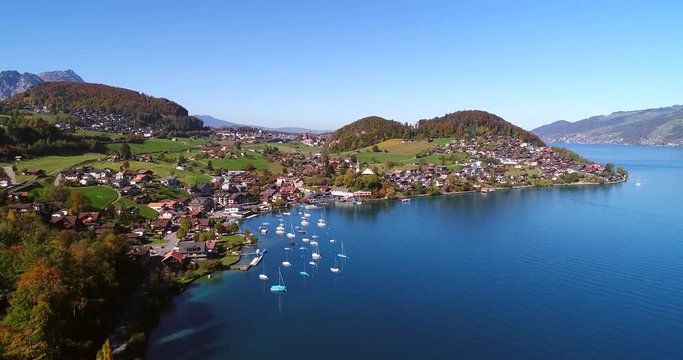 own at a lake, Cinema 4k aerial view of a colorful autumn color city spiez, on a sunny fall day, in berner oberland, in the alps of switzerland