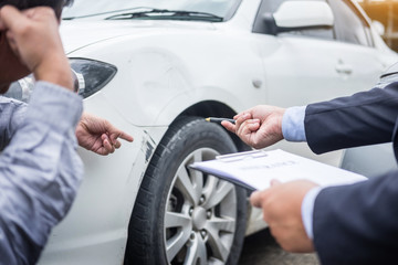 Insurance agent writing on clipboard while examining car after accident claim being assessed and...