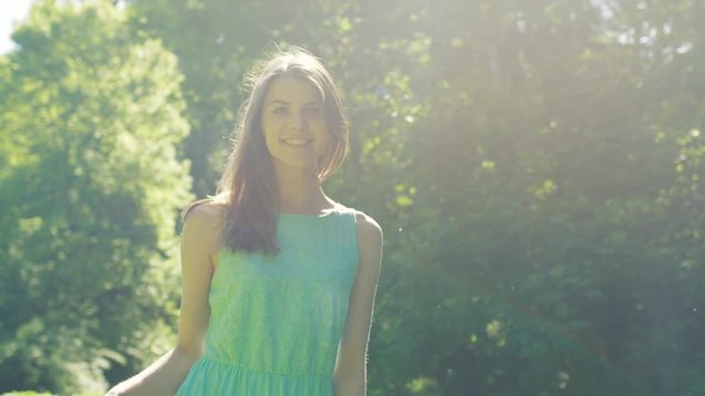 Portrait shot of the beautiful young woman with long hair and in green dress spinning in the beautiful green sunny park in summer. Outside