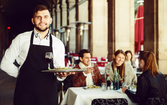 smiling waiter with serving tray welcoming to restaurant