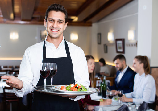 Portrait of smiling waiter with serving tray meeting restaurant guests