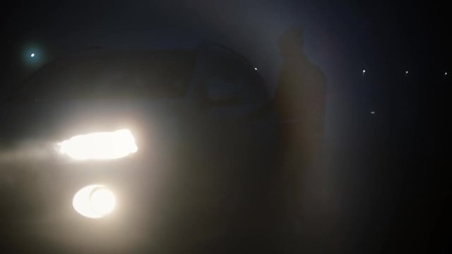 Abstract view. Female getting into a car at night. Blurry dark foggy bokeh highway background shot mysterious adventure.