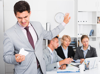 Irritated businessman in office with working associates
