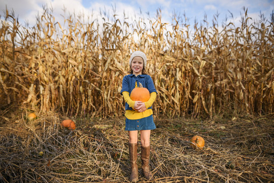 Girl standing in a pumpkin patch holding a pumpkin