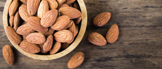 Almonds in brown bowl on textured wooden background.