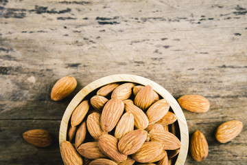 Almonds in brown bowl on textured wooden background.