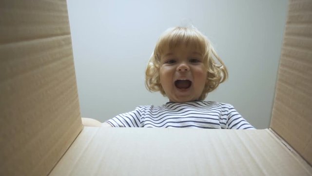 A little boy looks in the box, is surprised and happy to receive a surprise. The child opened a box with a gift. Slow Motion. Internet shopping.