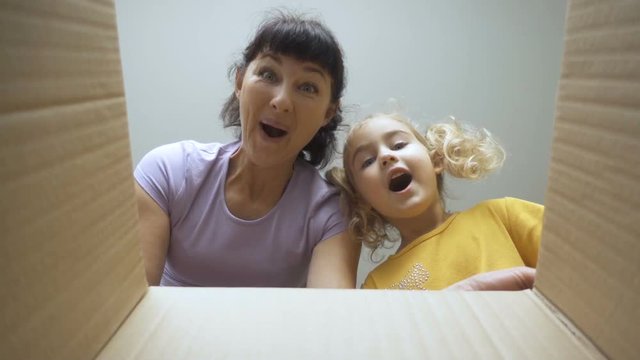 Mom and her daughter looks in the box, is surprised and happy to receive a surprise. Little Girl and woman opened a box with a gift. Slow Motion. Internet shopping.