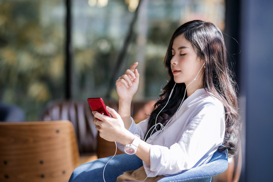 Young beautiful asian woman close her eyes and listening to music from smartphone while relax in cafe with happiness