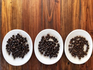 Touch the difference . Different of coffee beans roasts.roast coffee beans in the white dish on the brown wooden table, top view and copy space .