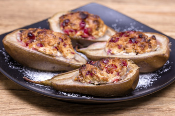 Homemade baked pears with cottage cheese, honey, red cranberries and walnuts in black plate on wooden background, healthy food