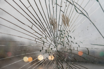 At the bus stop glass is broken. There are many cracks. Against the background of cars.