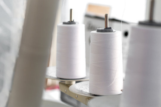 a spool of white thread stands on a dusty stand of sewing machine.