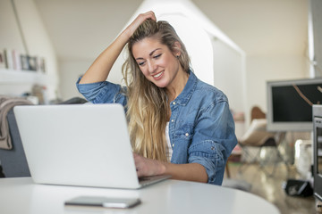 Young beautiful woman works for a computer from a home with a laptop on a white desk as a freelancer