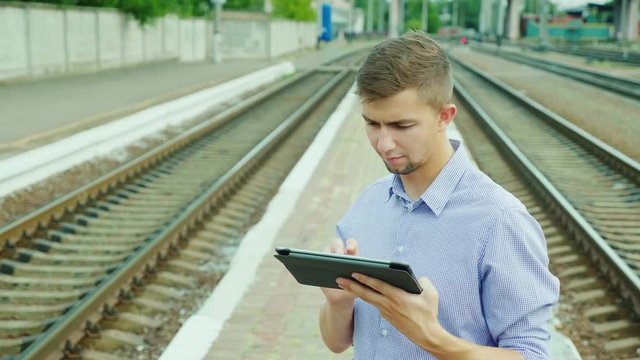 A young businessman uses a tablet at the train station. Waiting for the train