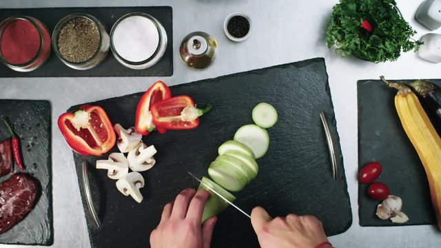 Top view of hands of unrecognizable cook slicing fresh zucchini with knife