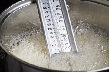 Candy thermometer close up in boiling liquid in metal pot