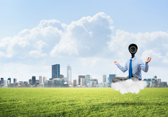 Camera headed man sitting in lotus pose on cloud against modern cityscape