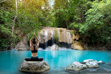 Beautiful woman practicing yoga on the rock in the beautifull waterfall.