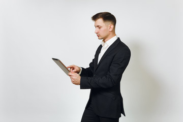 Young successful handsome rich business man in black suit working on modern tablet isolated on white background for advertising. Concept of money, achievement, career and wealth in 25-30 years.