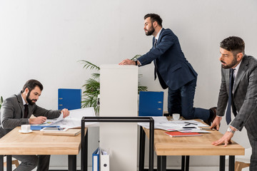 colleagues spying on businessman above partition in office