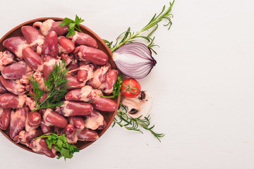 Raw chicken hearts on the plate ready for cooking with rosemary and spices on a white wooden background. Top view. Free space for text.