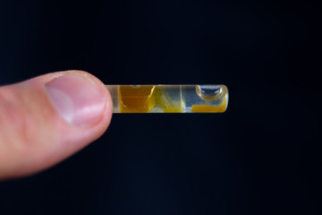 Medical Oil Cannabis - fingers holding apothecary test-tube with marijuana oil ready for use.