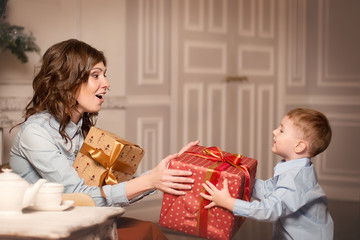 A young mother with an emotion of surprise receives a Christmas gift from his son vintage beige interiors