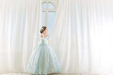 Elegant woman at a high window in historic dress, straightens the curtains, waiting friends