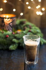 Coffee in a glass on a table and glowing Christmas tree on a dark background