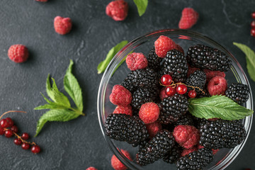 Top view photo on a glass plate with ripe red blackberries, raspberries, currant and green mint leaves on a black surface. Macro photo of ripe blackberries, raspberries and berries of currant.