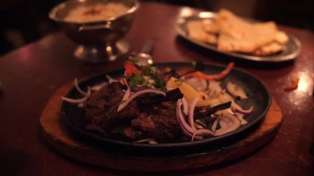 Tandoori lamb dish in Indian restaurant. A woman's hand forks a piece of meat.