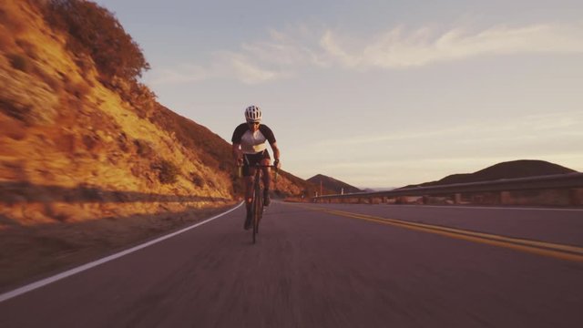 Young Fit Man Cycling On Road Bike Outside At Sunset Up Hill