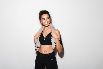 Smiling curly brunette fitness woman with towel listening music