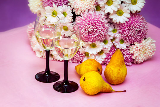 Two elegant glasses of white fruit wine or champagne and ripe yellow pears on the table with beautiful aster and chrysanthemum flowers bouquet on background.