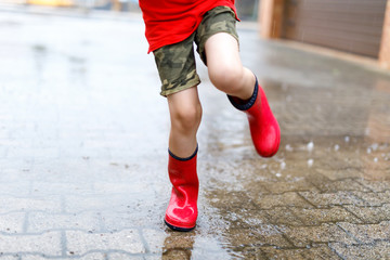 Fototapeta na wymiar Child wearing red rain boots jumping into a puddle.