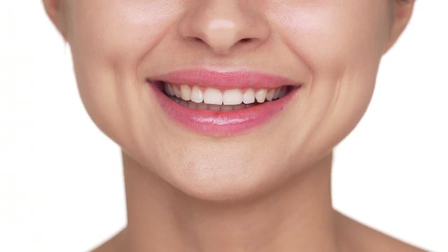 Extreme closeup portrait of young woman wearing light fresh lip make-up smiling showing her healthy perfect teeth after dentist appointment over white background