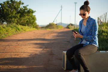 Woman using her mobile phone while sitting on suitcase