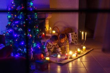 Two little children sitting by a fireplace at home on Christmas