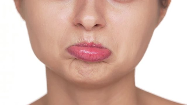 Macro view of adult woman with healthy clean skin and natural makeup twisting her lips being upset or offended over white background. Facial expressions