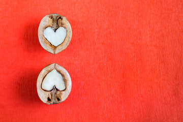 Two halves of walnut in shape of heart are lying over one another on red textured paper.