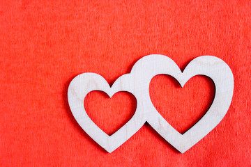 Two carved wooden hearts are lying on red textured paper background and copy space.